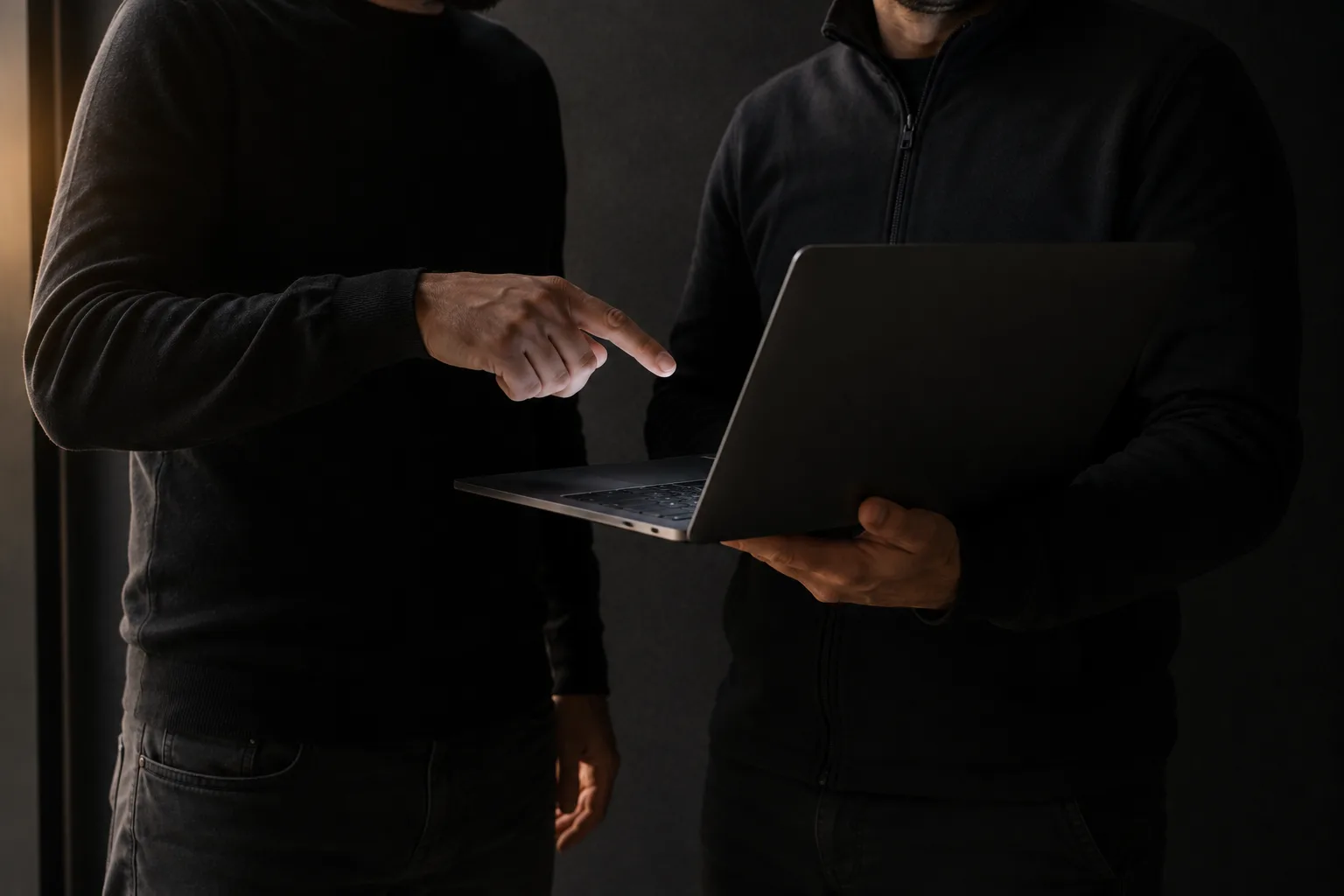 Zwei stehende Personen, auf Oberkörperhöhe angeschnitten; die eine hält einen geöffneten Laptop, die andere zeigt auf eine Stelle des Bildschirms.